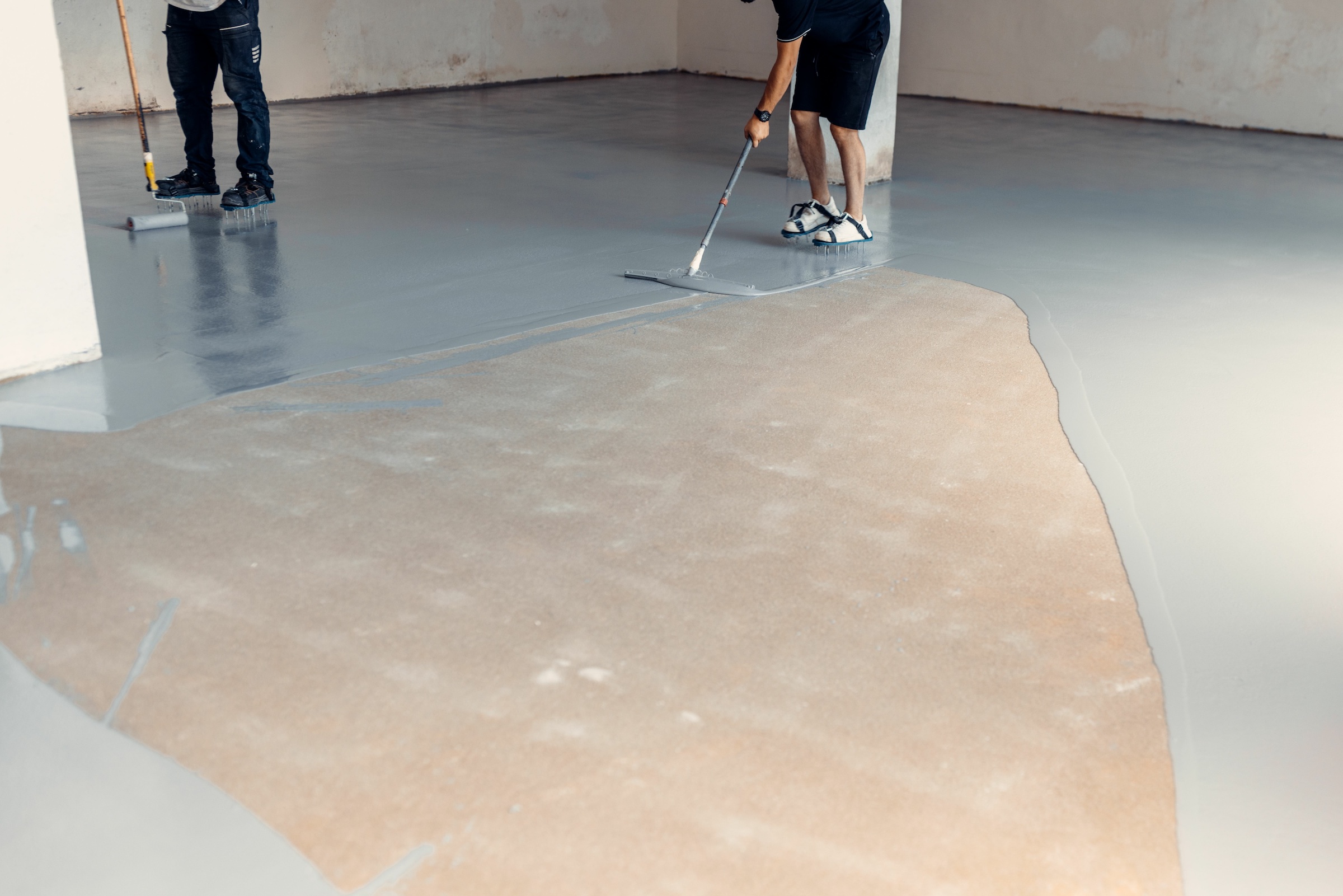 Construction workers applying grey epoxy resin in an industrial hall
